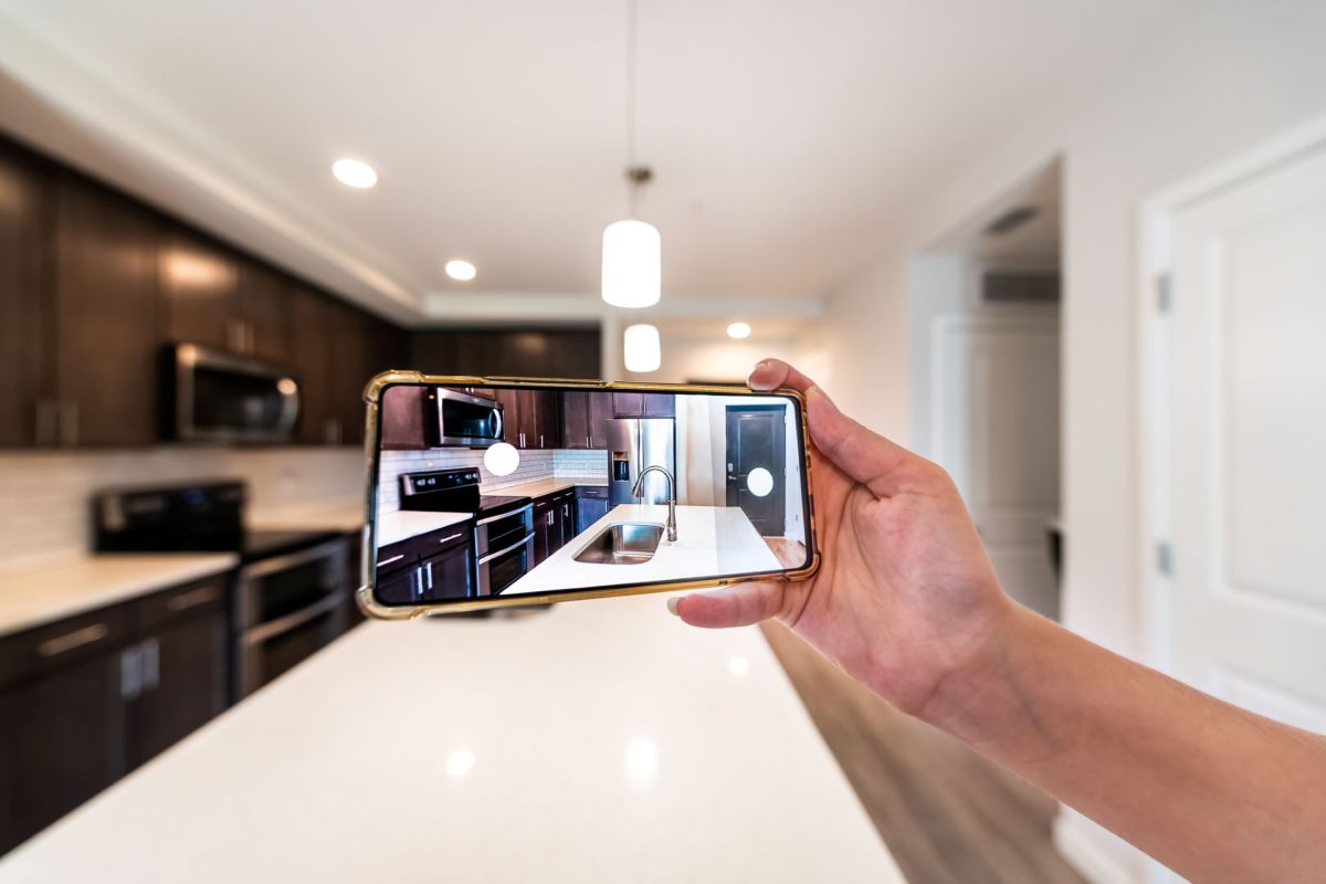 A person using a cellphone to take photos of a kitchen.