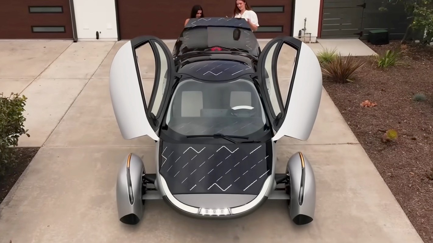 An Aptera electric car with solar panels on its roof and hood, with its doors open and pointing up