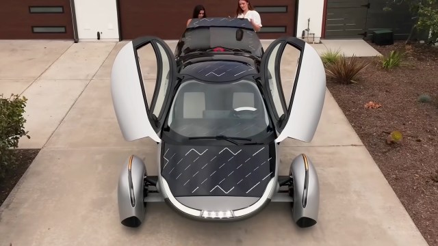 An Aptera electric car with solar panels on its roof and hood, with its doors open and pointing up