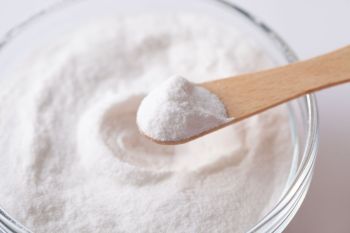 A spoon has a scoop of artificial sweetener over a bowl