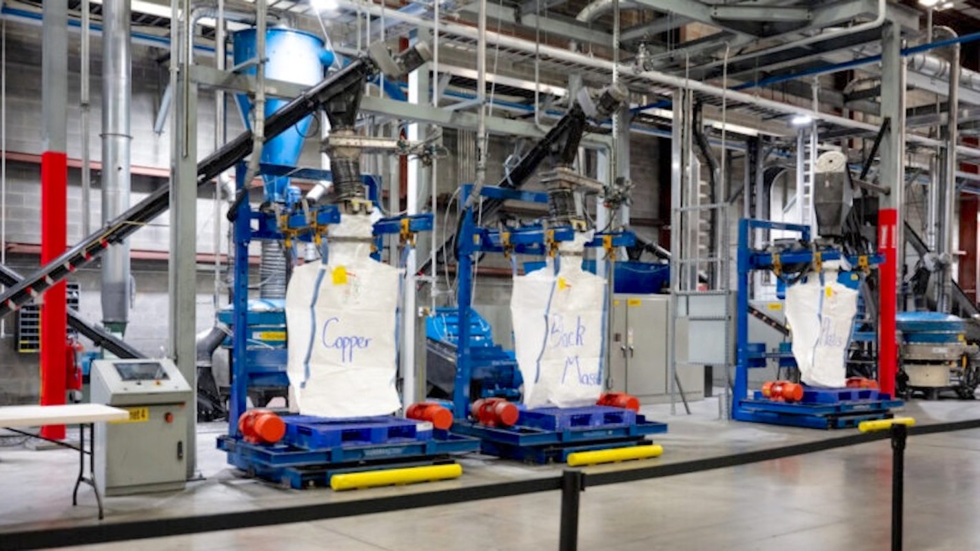 Industrial machinery with bags labeled "Copper," "Black Mass," and "Plastic" in a factory setting.