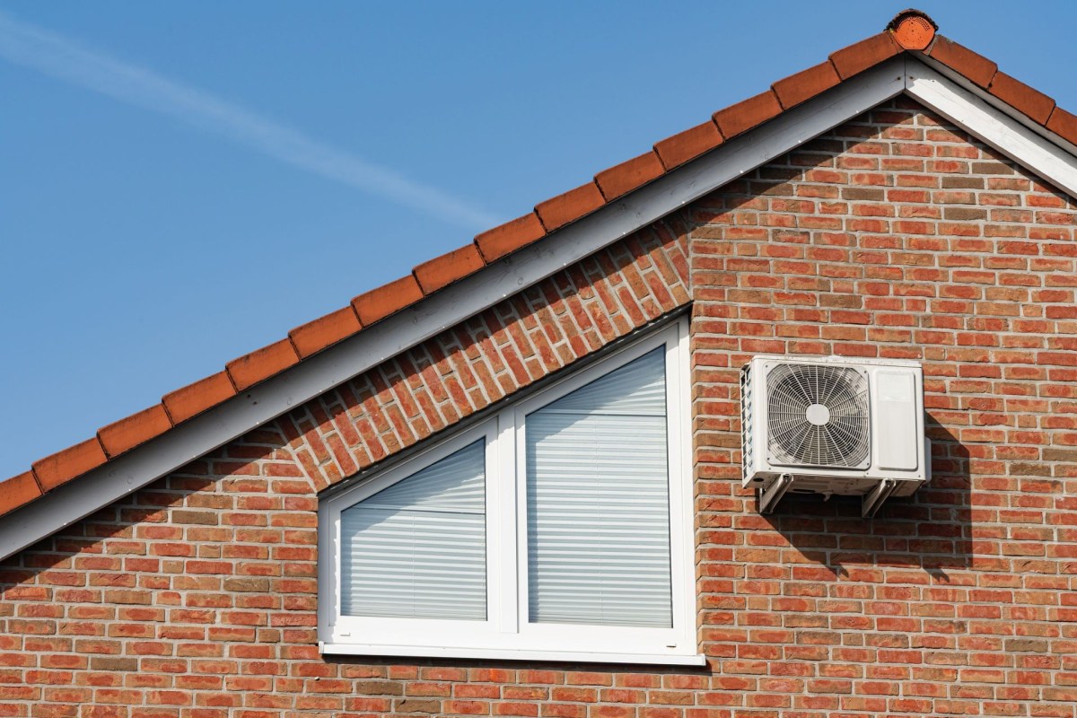 An outdoor AC unit is attached to the brick wall next to an attic window
