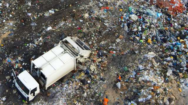 A garbage truck is on a waste pile, with workers collecting debris in a landfill area.