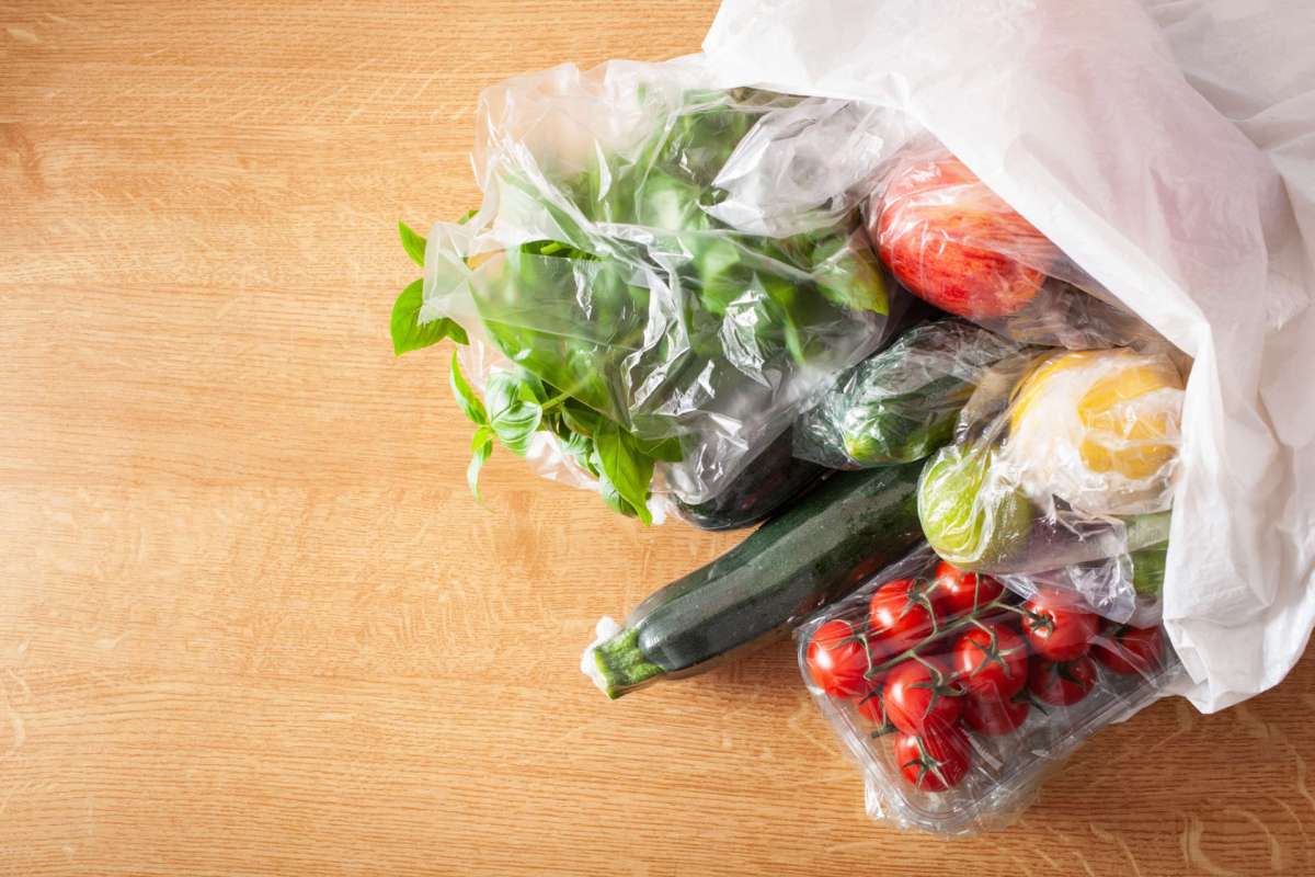 Various fresh vegetables and fruits in plastic bags on a wooden surface.
