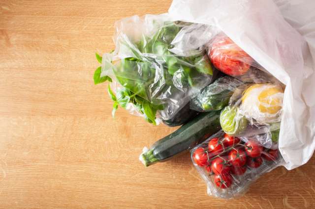 Various fresh vegetables and fruits in plastic bags on a wooden surface.