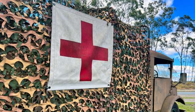 A military vehicle covered in camouflage netting with a red cross symbol displayed prominently.