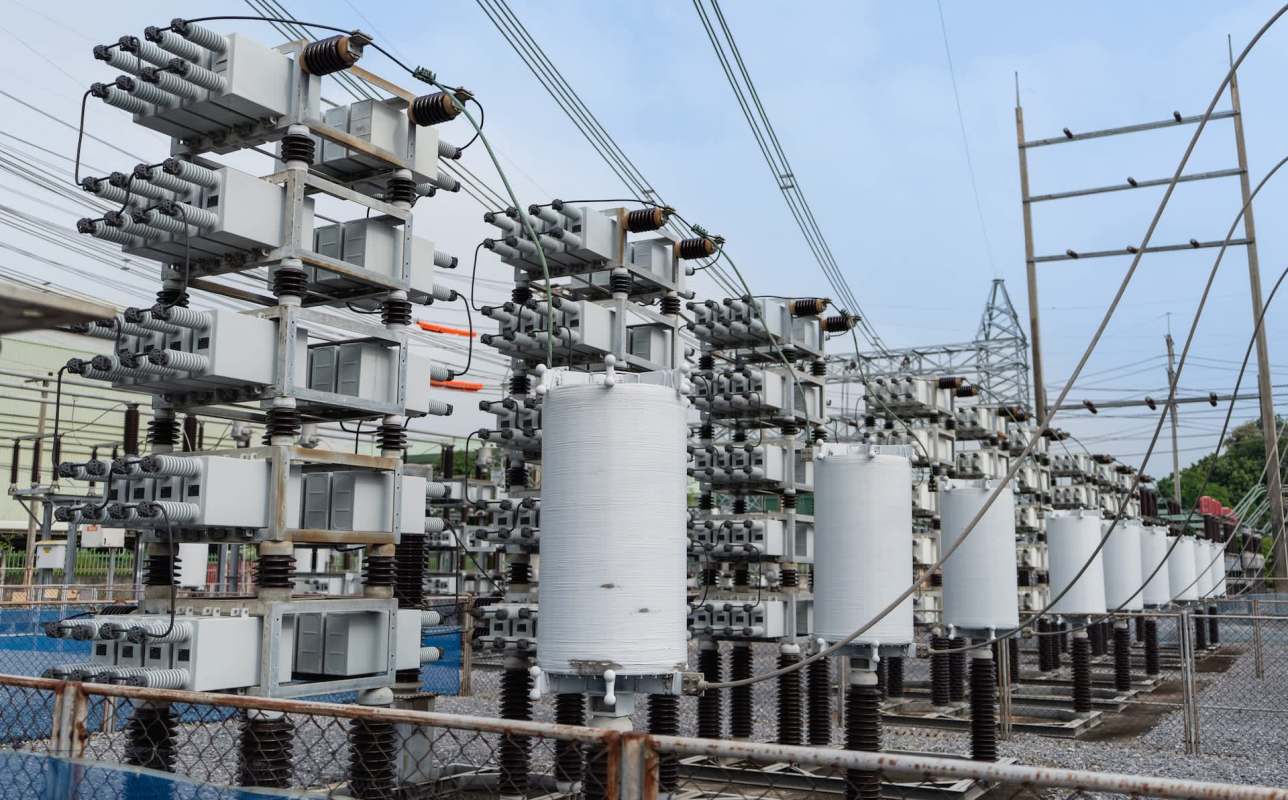 An electrical substation featuring multiple gray transformers and insulators against a cloudy sky.