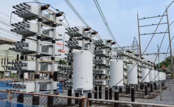 An electrical substation featuring multiple gray transformers and insulators against a cloudy sky.
