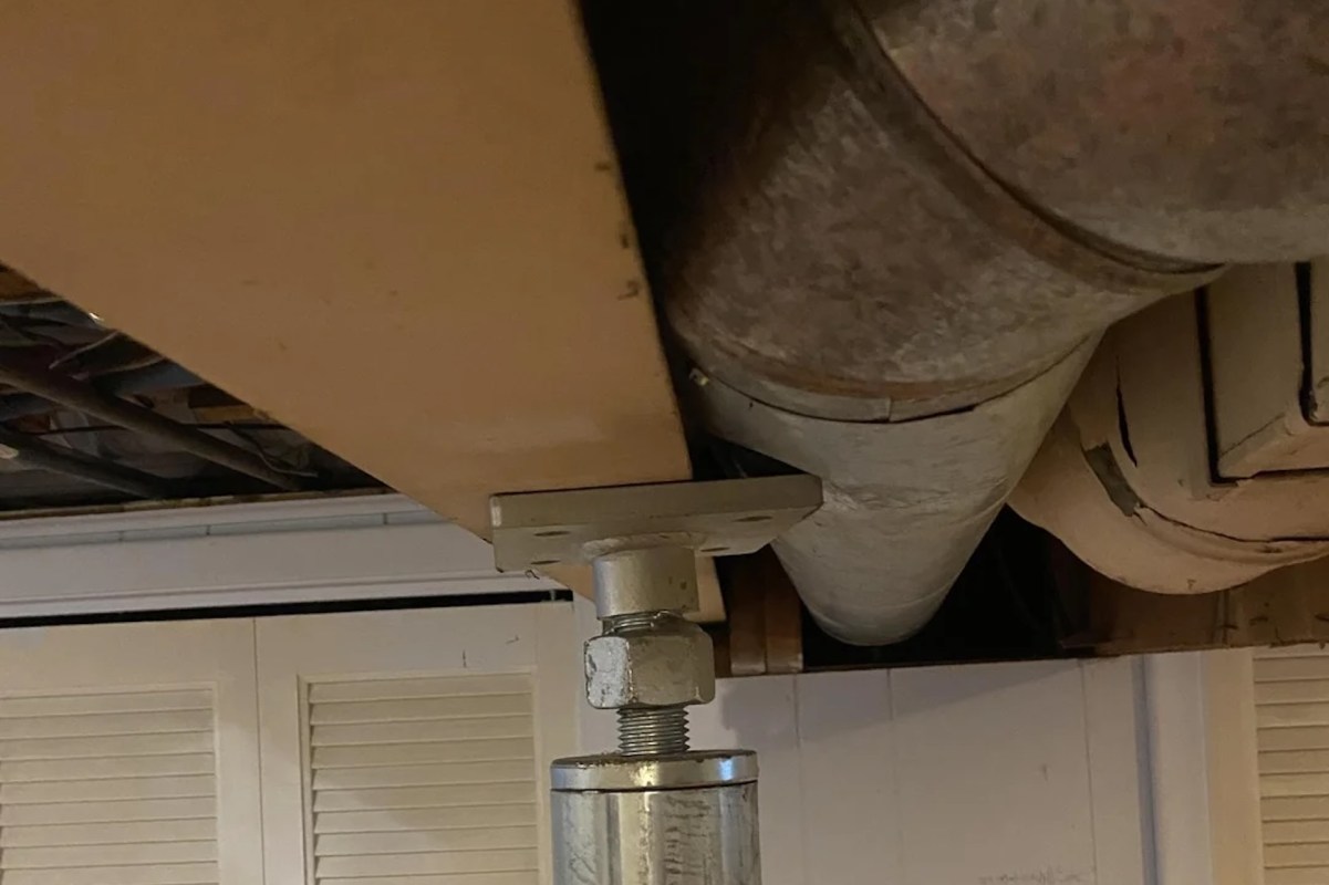 A metal support bracket holding a pipe beneath a wooden surface in a basement setting.