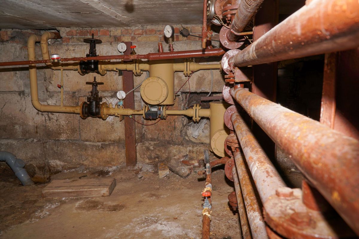 a basement with a brick wall and dirt floors with old pipes on the wall