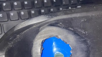 A worn object with a circular hole revealing a blue surface, set against a blurred keyboard background.