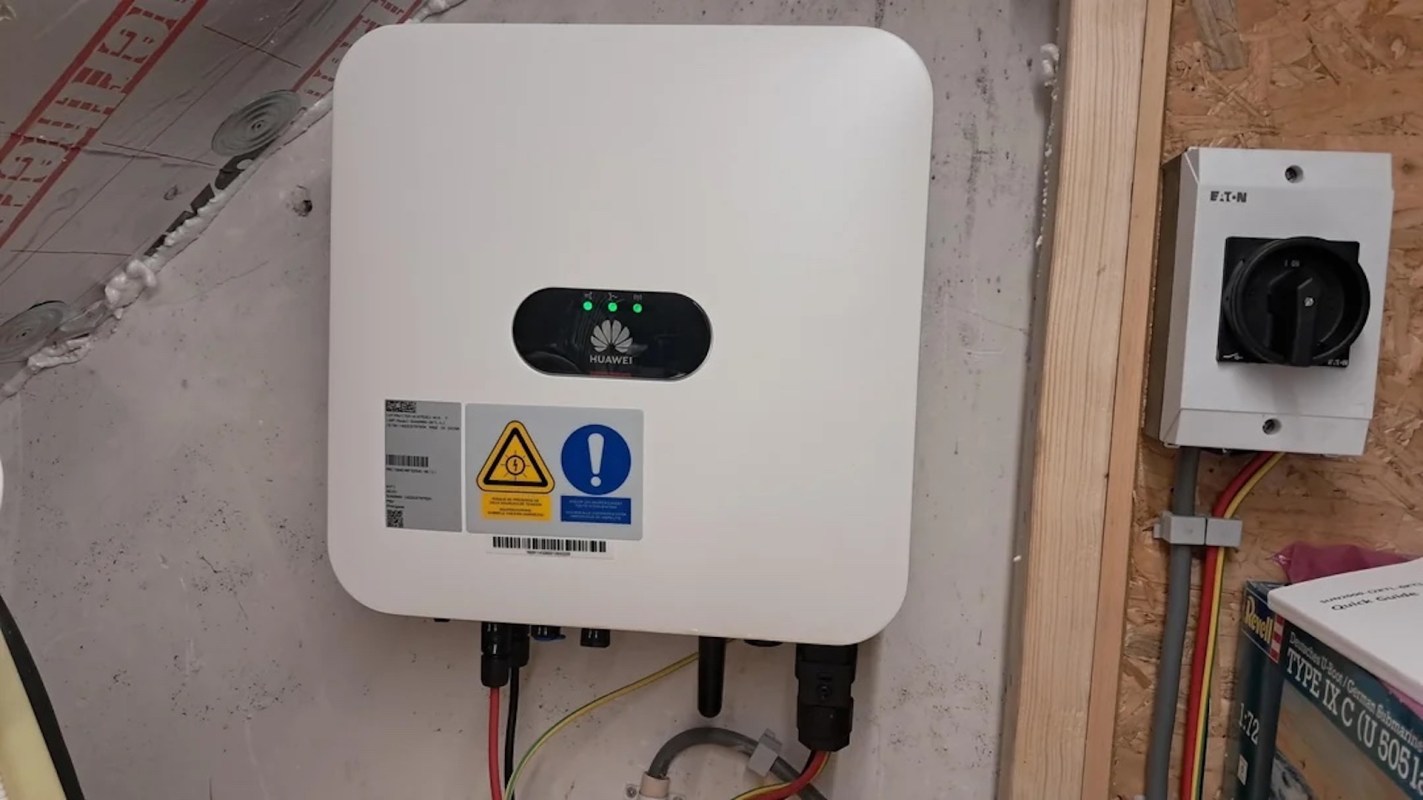 A Huawei inverter mounted on a wall with warning labels and electrical connections.
