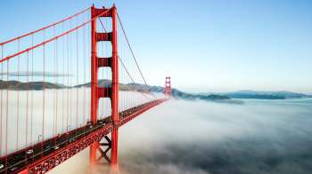 The Golden Gate Bridge partially obscured by fog, with vehicles on the roadway and hills in the background.
