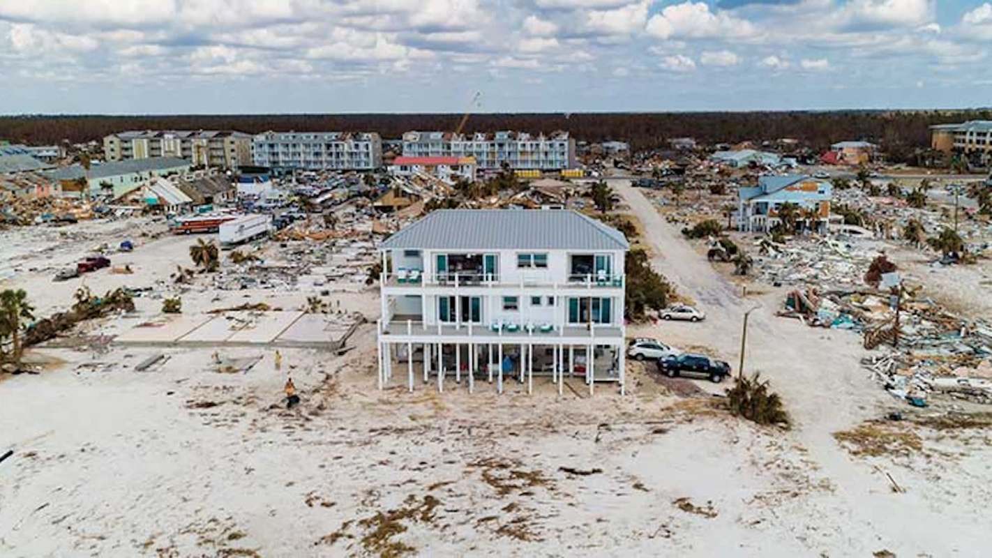 A two-story house stands amid a landscape of debris and damaged buildings.