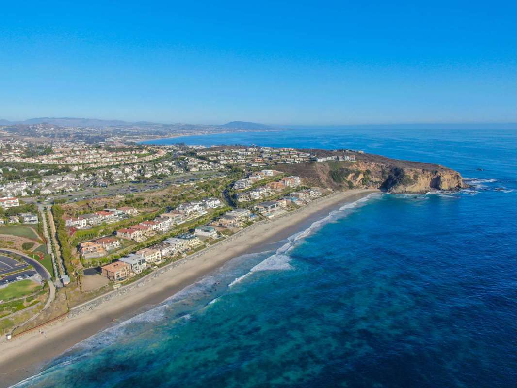A coastal view showcasing a beach, houses, and the ocean under a clear blue sky.