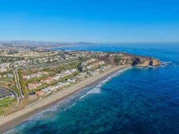 A coastal view showcasing a beach, houses, and the ocean under a clear blue sky.