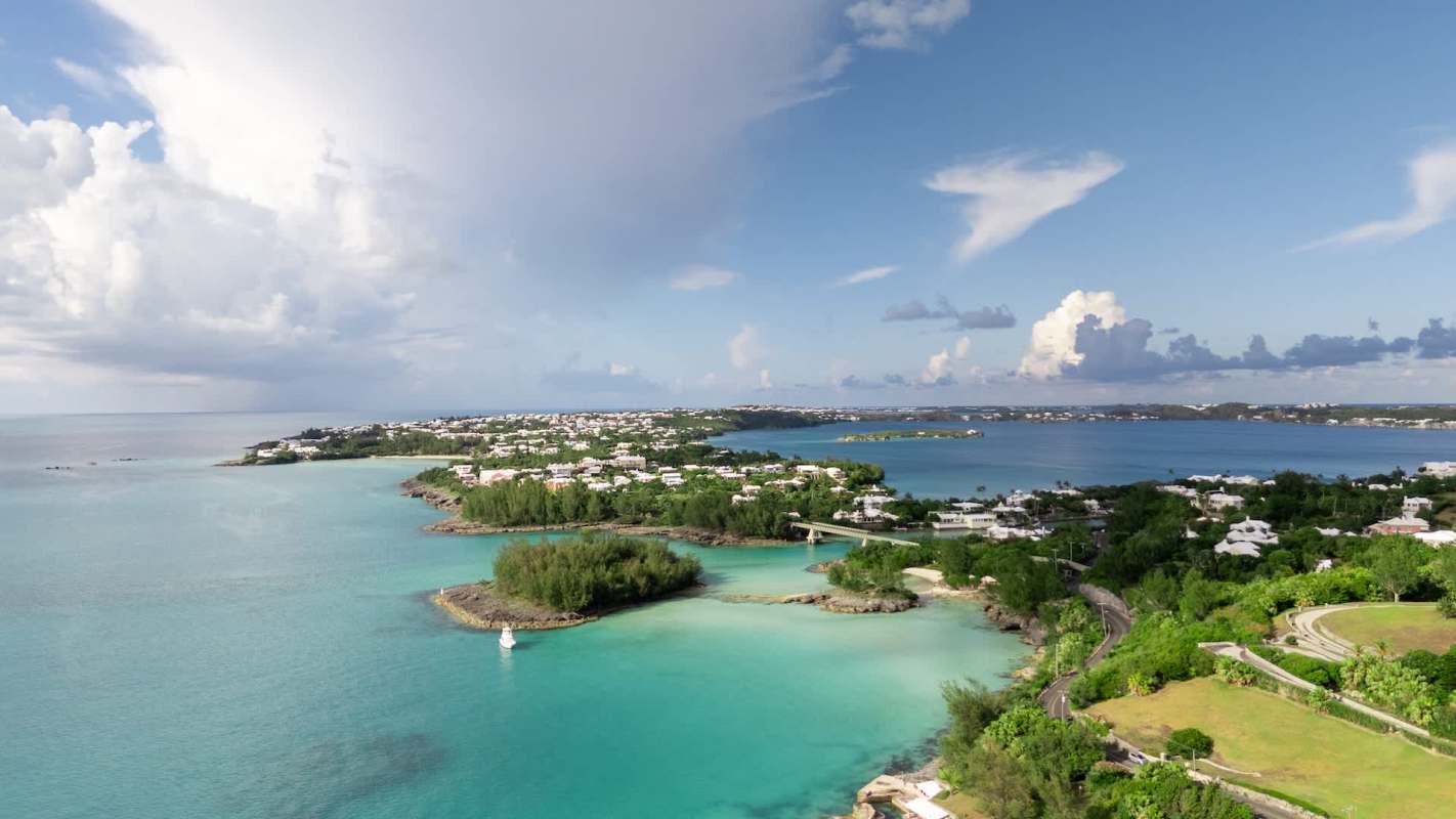 A coastal view featuring turquoise waters, green vegetation, and residential areas under a blue sky with clouds.