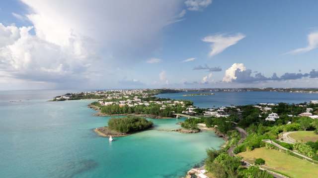 A coastal view featuring turquoise waters, green vegetation, and residential areas under a blue sky with clouds.