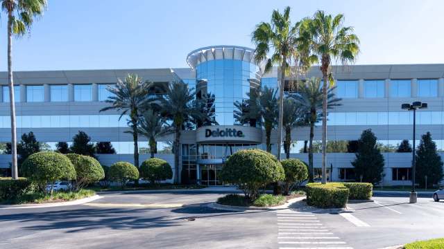 An office building with the Deloitte logo, surrounded by palm trees and manicured hedges.