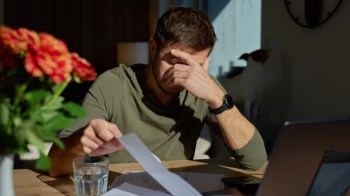 A man with his hand on his head reviews documents at a table.