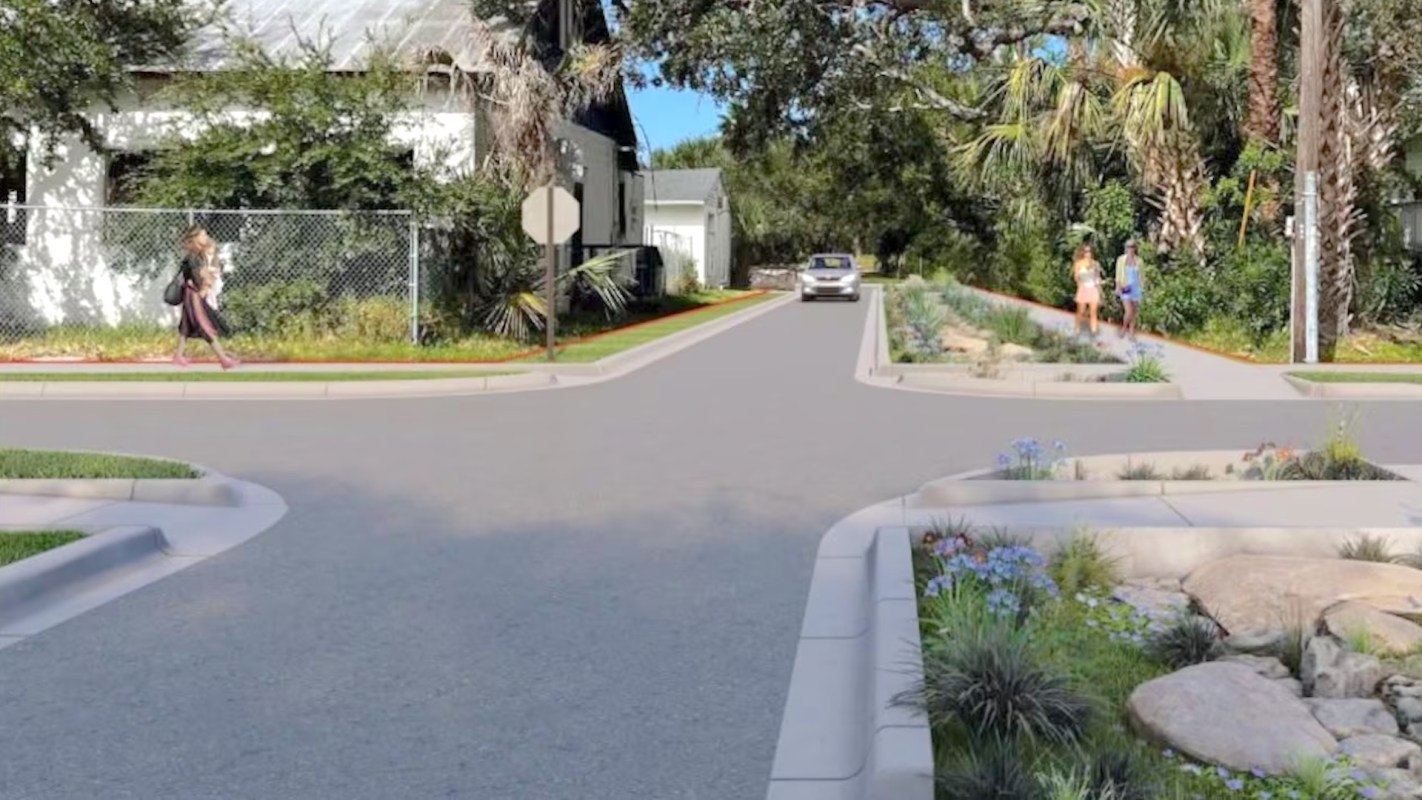A street scene featuring pedestrians walking, landscaped areas, and a car approaching an intersection.