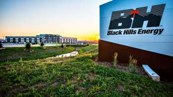 A sign for Black Hills Energy near a modern building at sunset, with grass and a small stream in the foreground.
