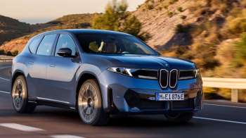 A blue BMW SUV drives on a winding road with rocky hills in the background.