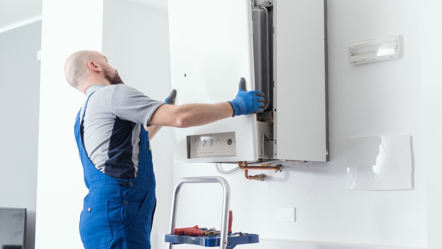 A technician installs a boiler on a wall, using tools from a nearby cart.