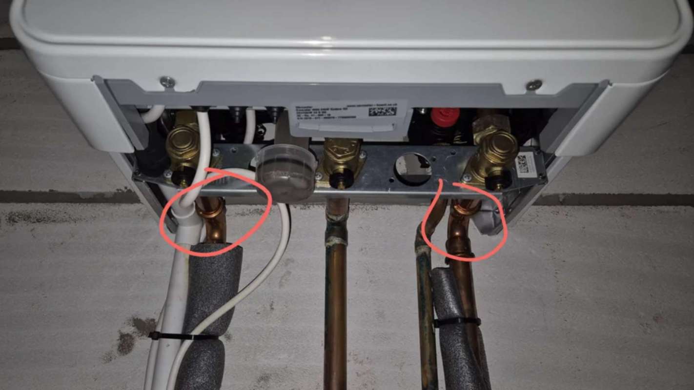 A person using a wrench to tighten a yellow pipe fitting connected to wall-mounted valves.