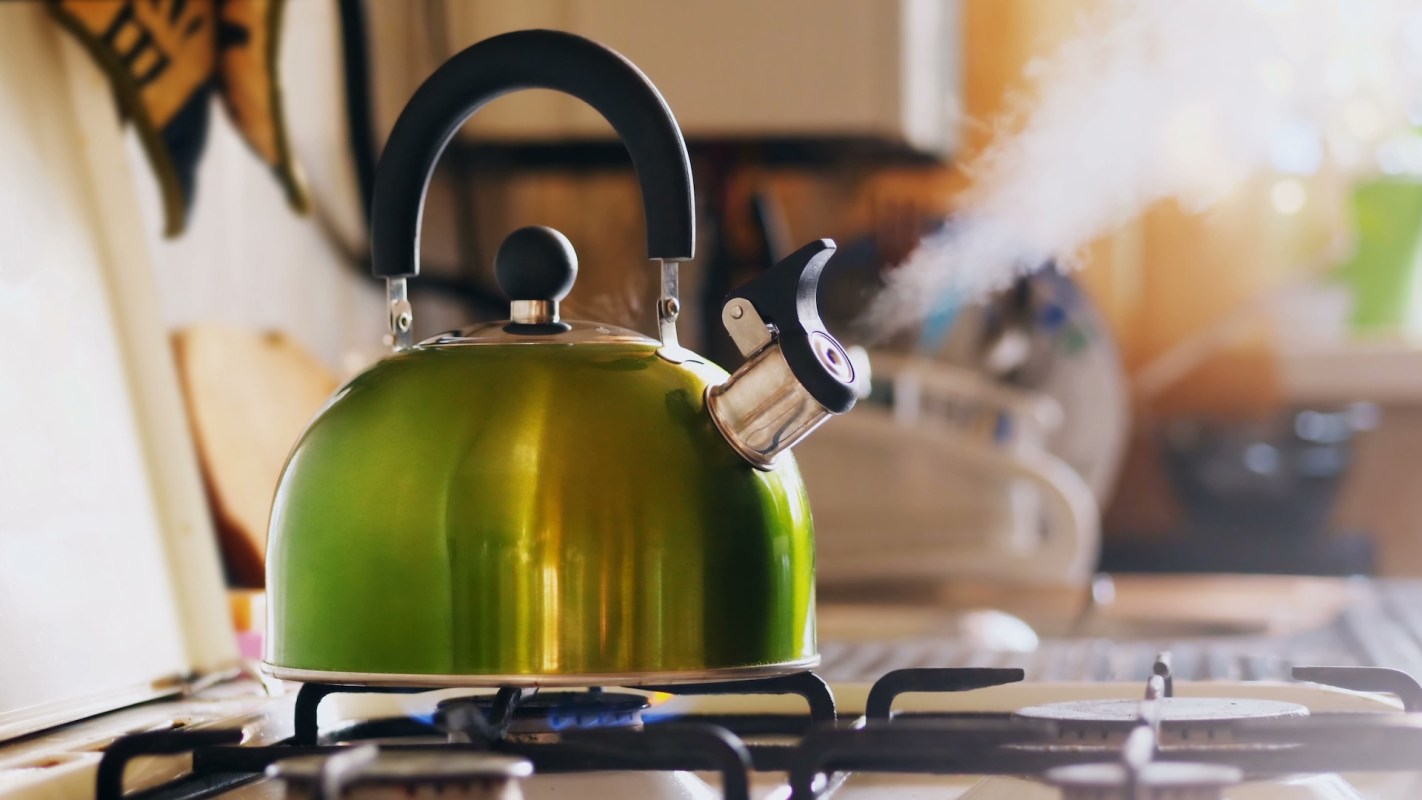 A green kettle on a gas stove with steam rising from the spout.