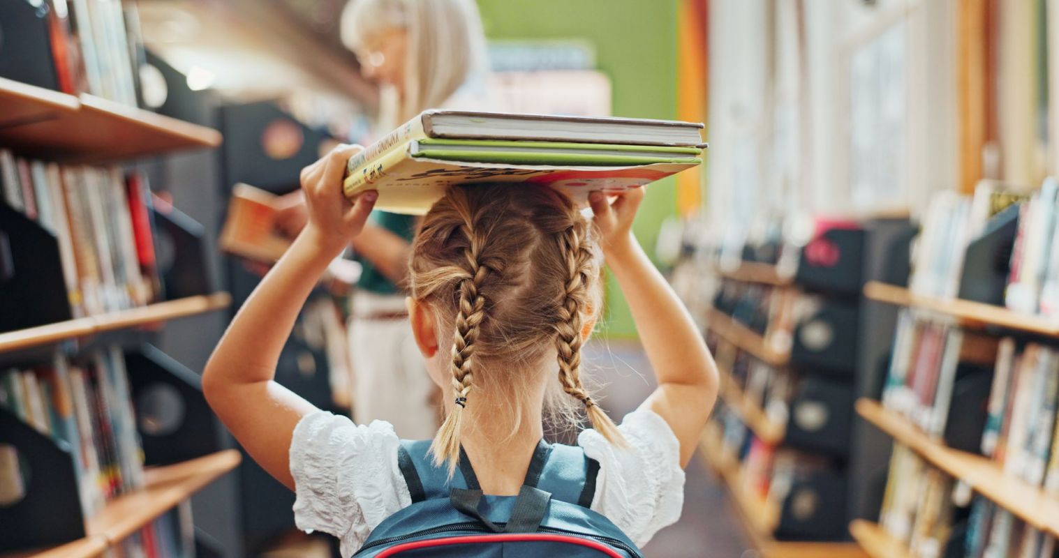 A kid carrying a couple of books on her head.