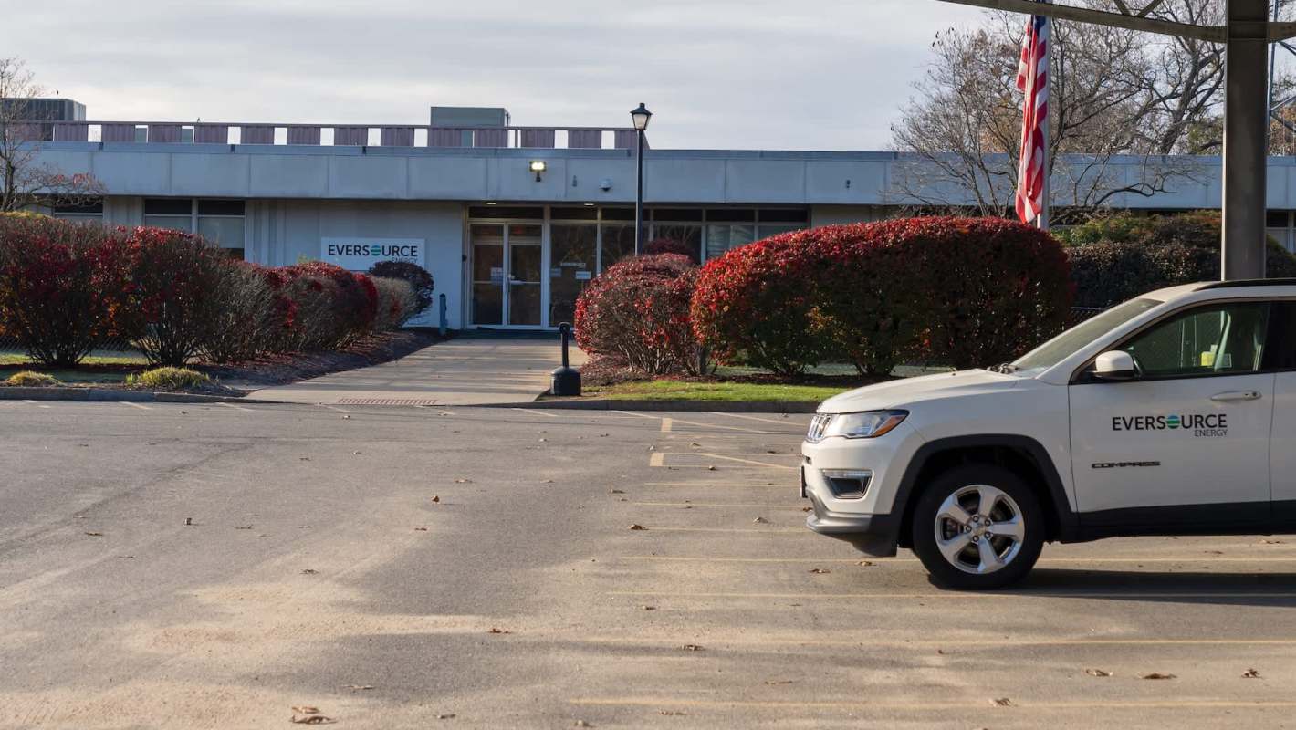 A parked Eversource vehicle in front of an Eversource building with red bushes and an American flag.