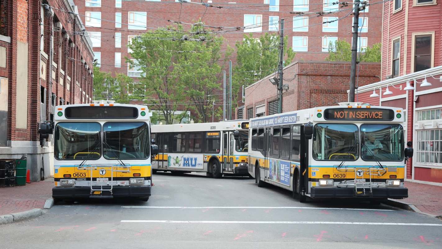 Three Boston MBTA buses are parked in an urban area, with one displaying "NOT IN SERVICE."