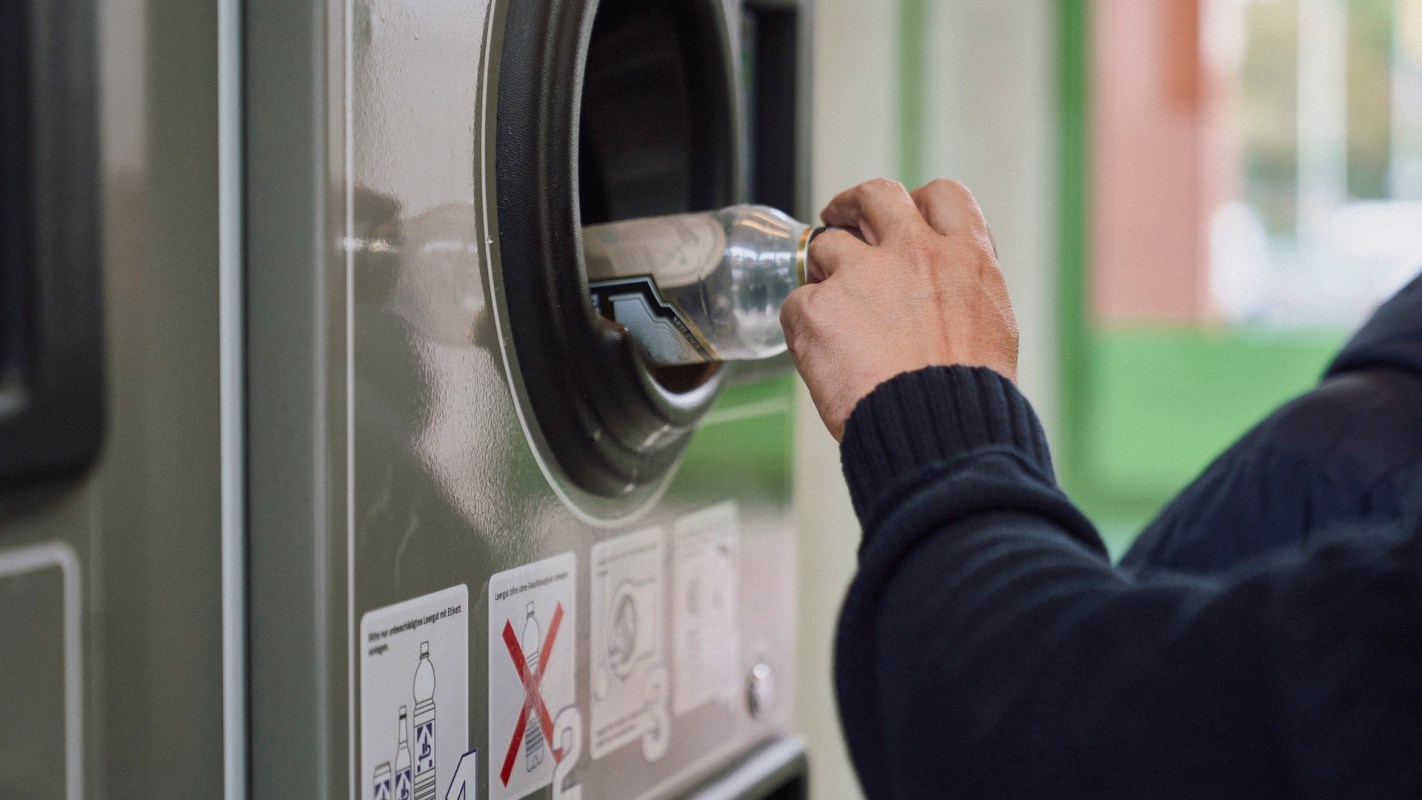 A person inserts a plastic bottle into a recycling machine.