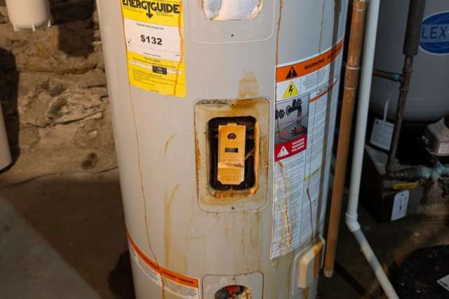 A water heater with rust and stains, displaying warning labels and an EnergyGuide sticker.