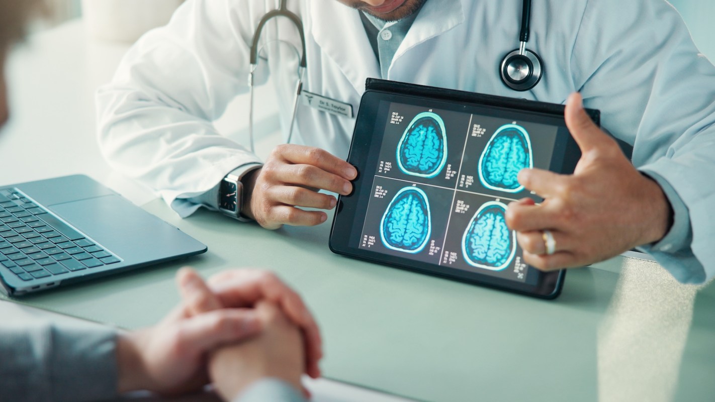 A doctor shows brain scans on a tablet to a patient during a consultation.