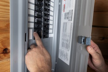 A man's hand toggles breakers inside a breaker box