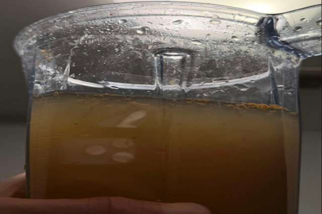 A blender pitcher filled with a brown liquid and sediment at the top.