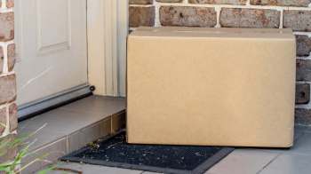 A cardboard box sits on a doorstep next to a welcome mat.