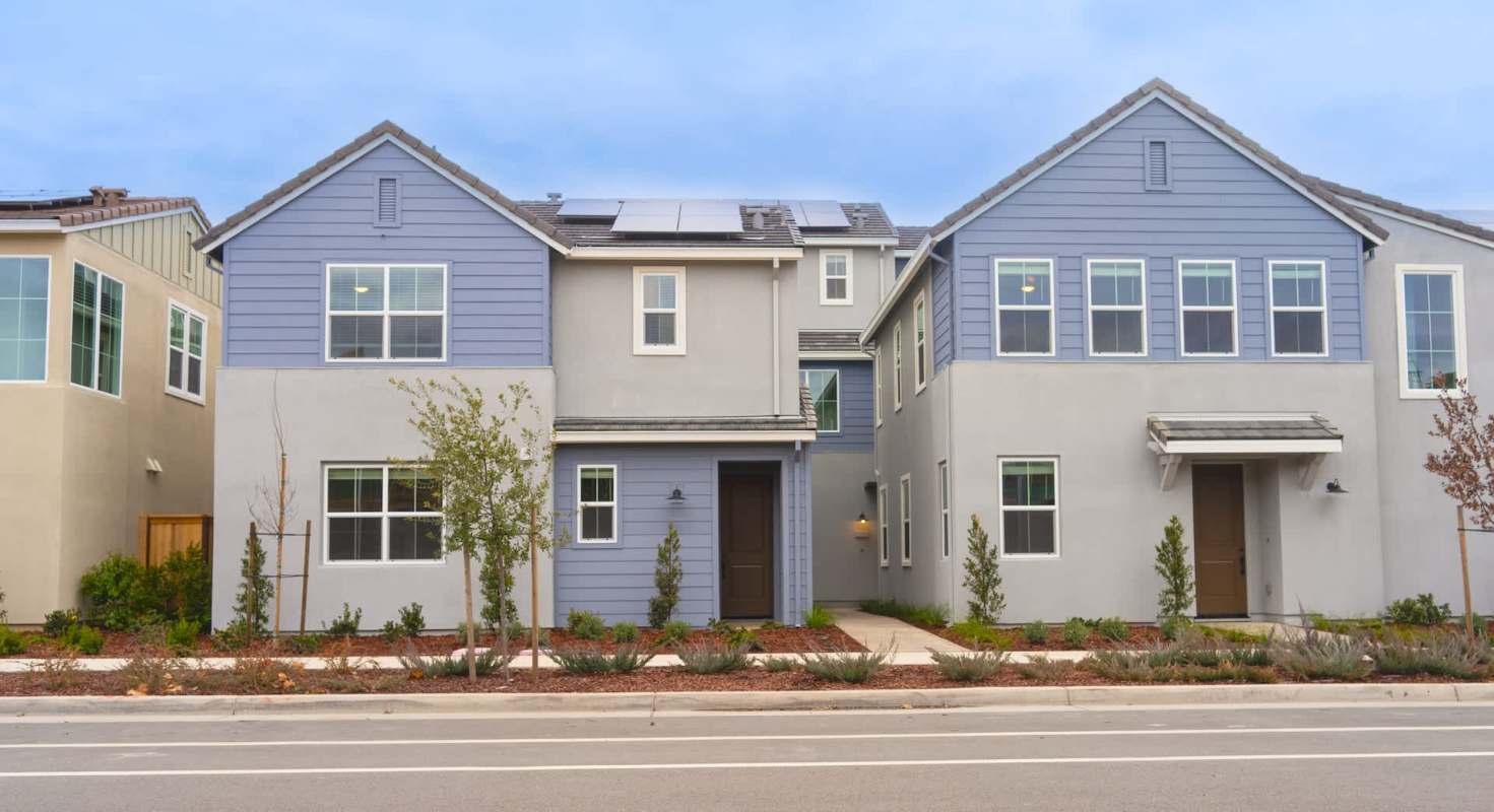 Two modern residential townhouses with landscaped front yards and a sidewalk.