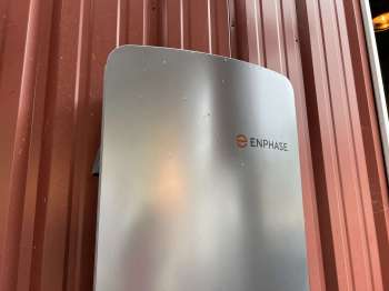 An Enphase device mounted on a red metal wall.