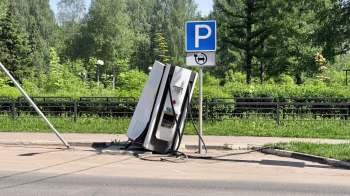 A broken, tilted electric vehicle charging station next to a parking sign in a green area.