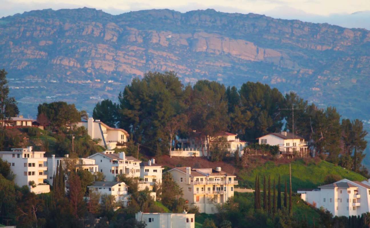 A hillside view featuring white houses and greenery, with a mountain in the background.
