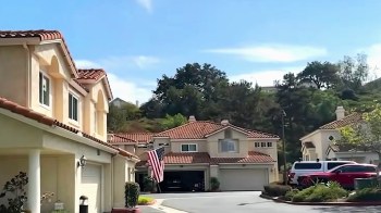 Residential neighborhood with houses, American flag, and parked vehicles under a clear blue sky.