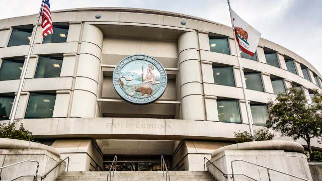 The exterior of a government building featuring the Great Seal of California and American flags.