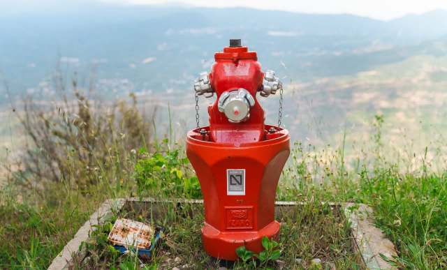 A red fire hydrant surrounded by grass and a distant landscape.