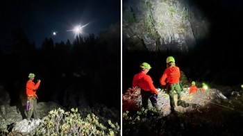 A group of climbers in safety gear work during the night near a rocky area, illuminated by headlamps.