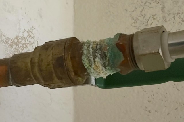 A corroded pipe joint with green buildup attached to a copper pipe.
