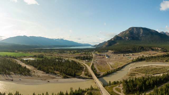 A panoramic view of mountains, a river, and a town surrounded by forests and fields.