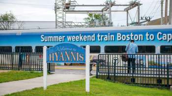 A sign welcomes visitors to Hyannis next to a train advertising services to Cape Cod from Boston.
